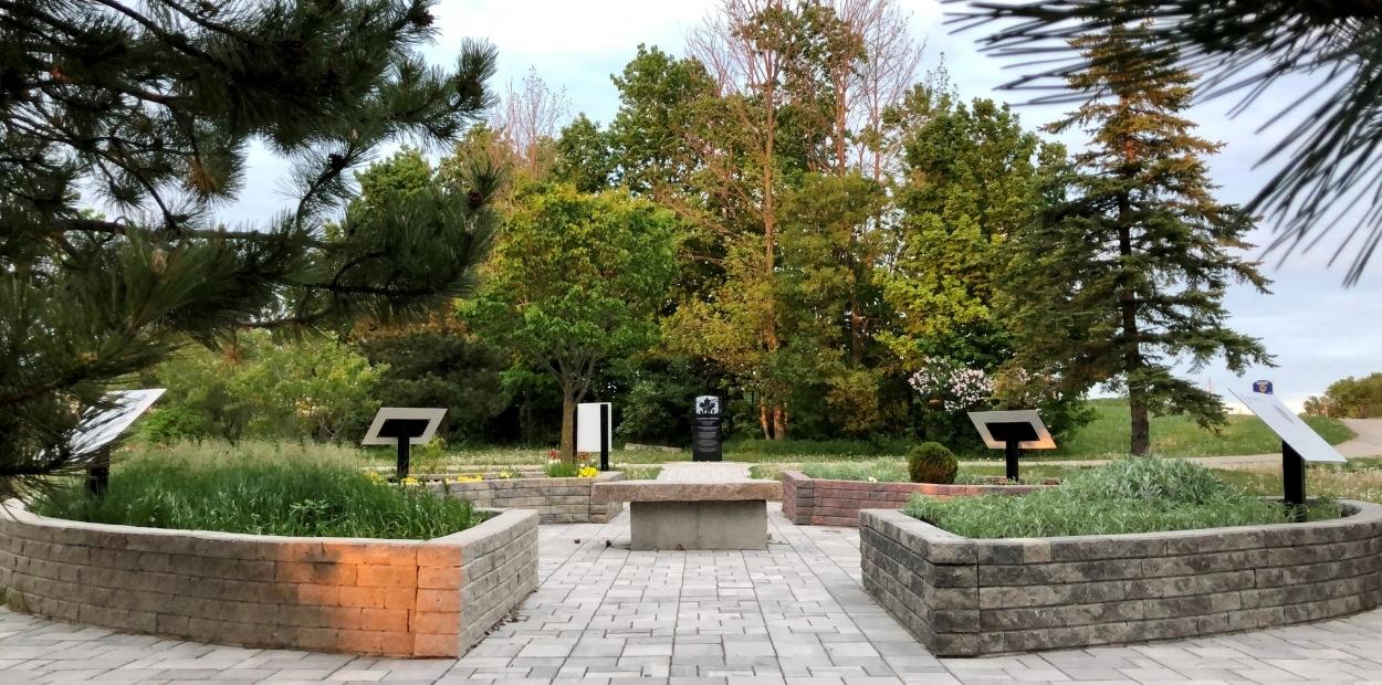 Garden with four raised beds arranged in a circle surrounded by trees. A stone table sits in the middle of the circle. 